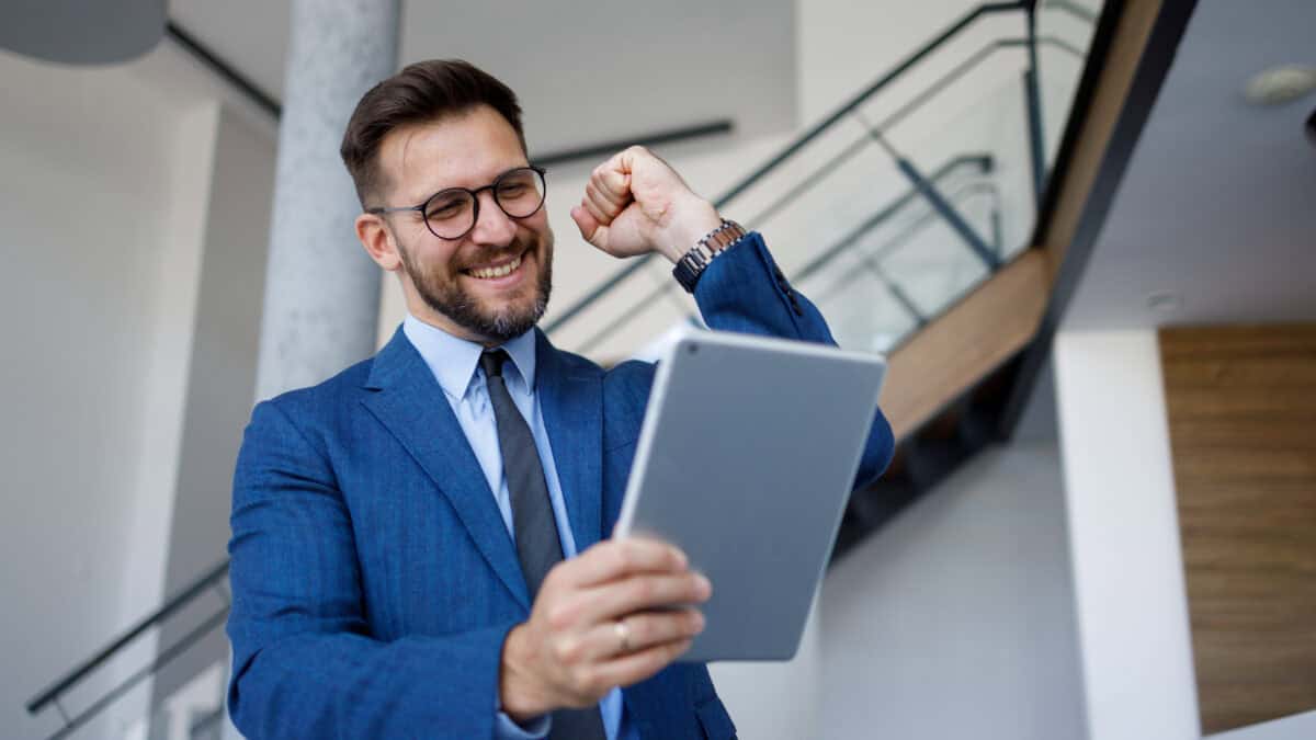 Happy businessman fist pumping while looking at a tablet.