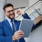 Happy businessman fist pumping while looking at a tablet.