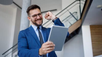Happy businessman fist pumping while looking at a tablet.