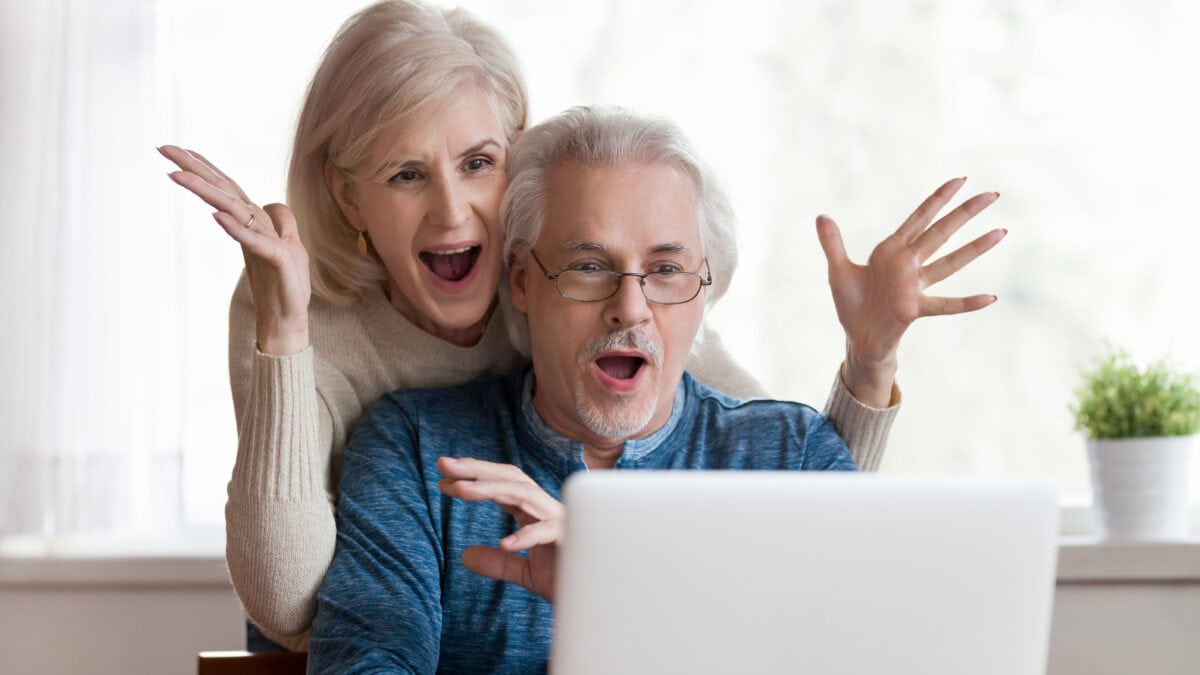 Mid-aged couple with surprised expressions on their face as they look at a laptop.