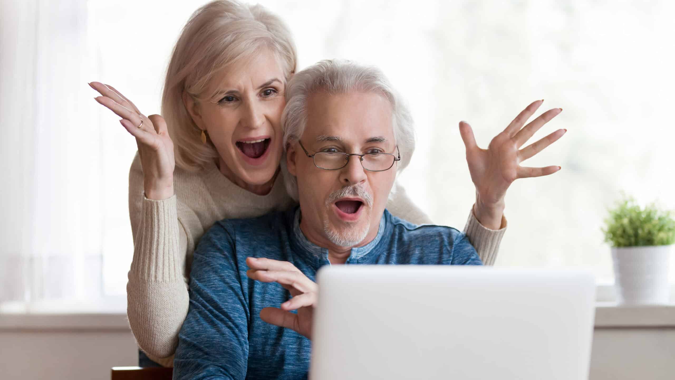 Mid-aged couple with surprised expressions on their face as they look at a laptop.
