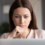 Woman looking at a laptop and thinking.