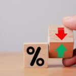 Hand flipping wooden cube block to change between up and down with percentage sign symbol next to it.