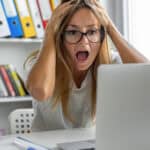 Woman screaming after looking at bad news on her laptop.