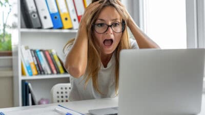 Woman screaming after looking at bad news on her laptop.