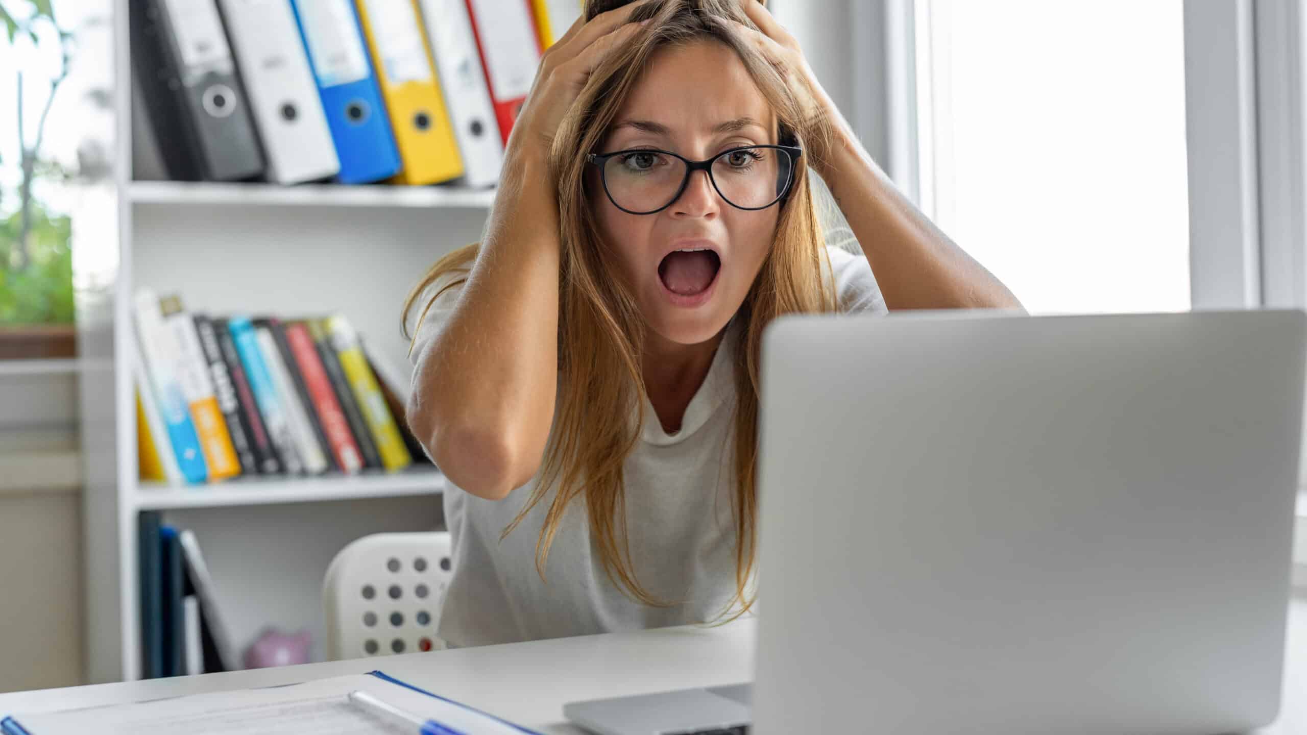 Woman screaming after looking at bad news on her laptop.