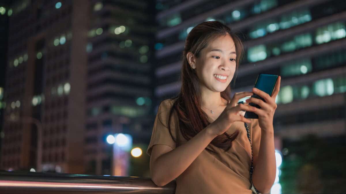 Happy woman looking at her phone, with buildings in the background.