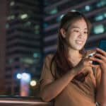 Happy woman looking at her phone, with buildings in the background.