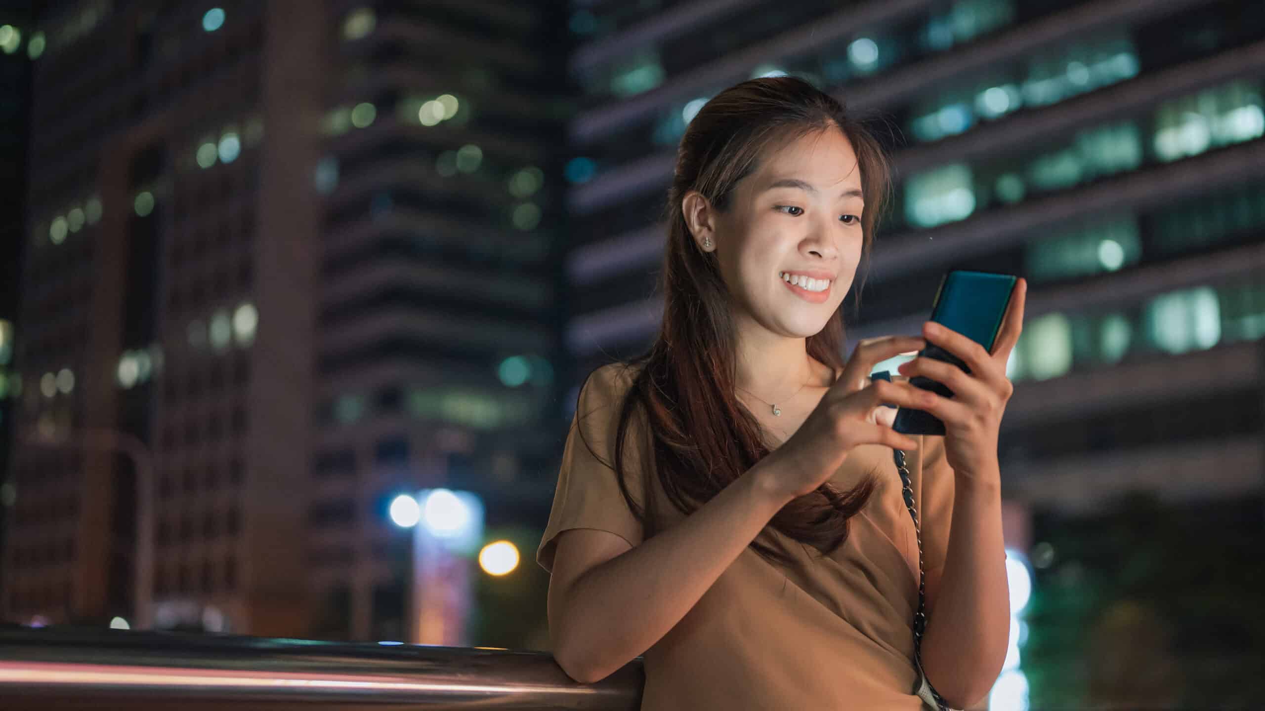 Happy woman looking at her phone, with buildings in the background.