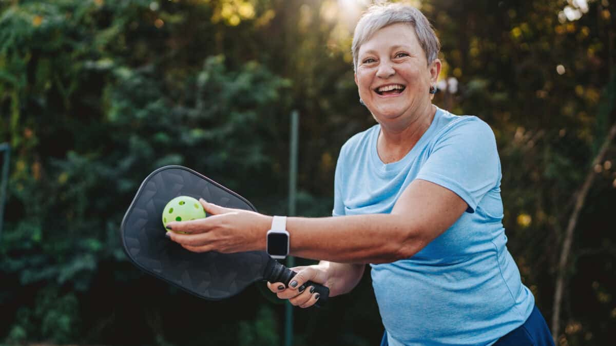 Happy and smiling retiree posing with pickleball and paddle.