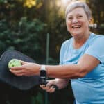 Happy and smiling retiree posing with pickleball and paddle.