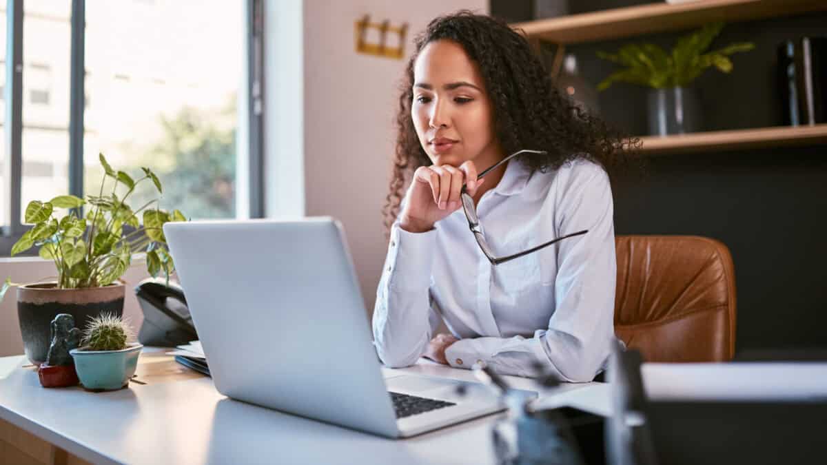 Woman holding her glasses and looking at her laptop.
