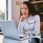 Woman holding her glasses and looking at her laptop.