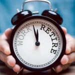 Person holding alarm clock with work and retire written.