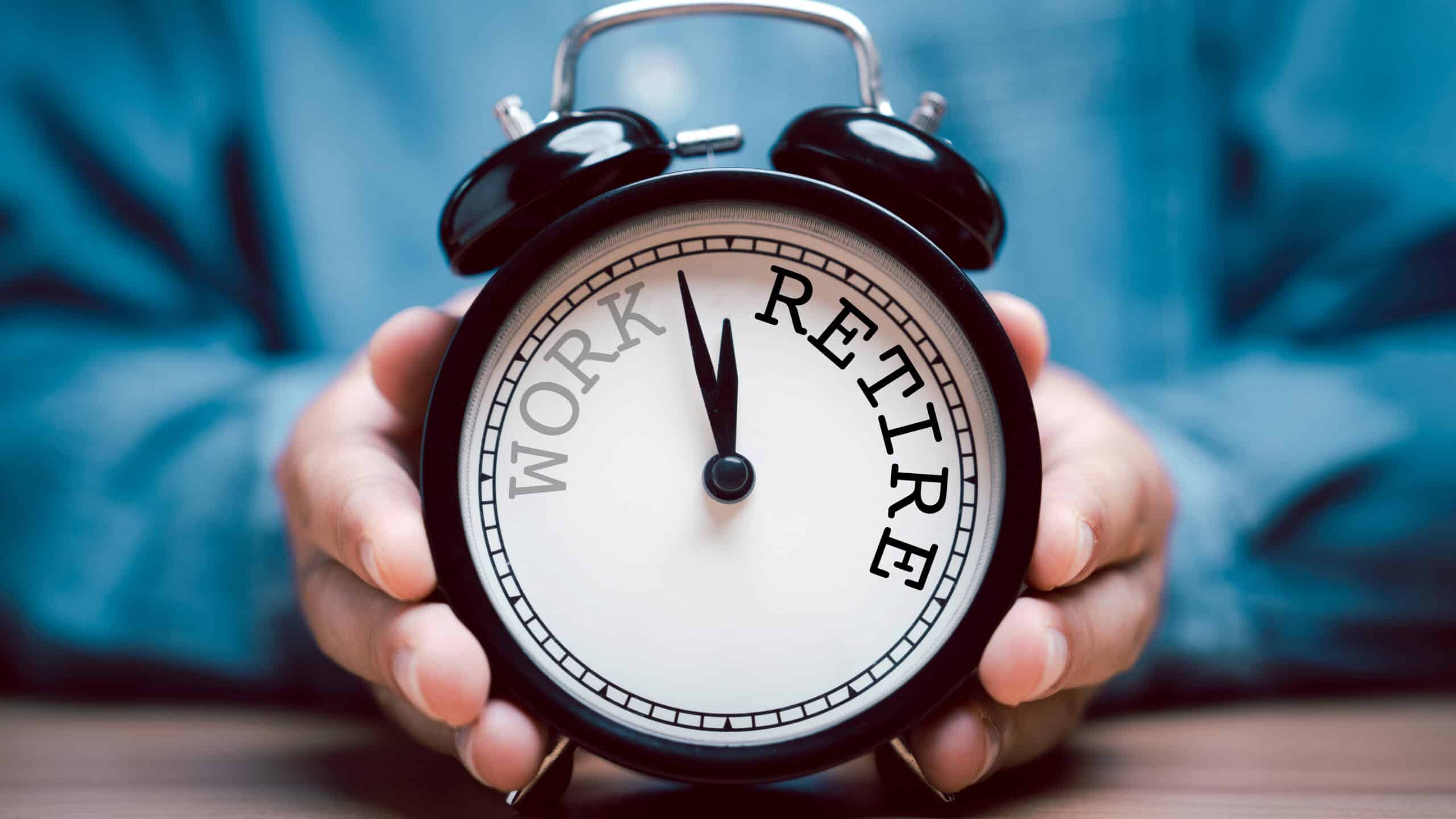 Person holding alarm clock with work and retire written.