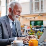 Old man working on his laptop at a cafe.