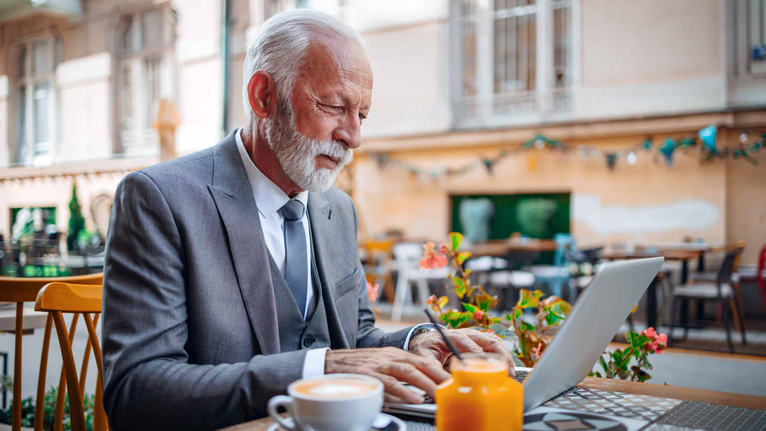 Old man working on his laptop at a cafe.