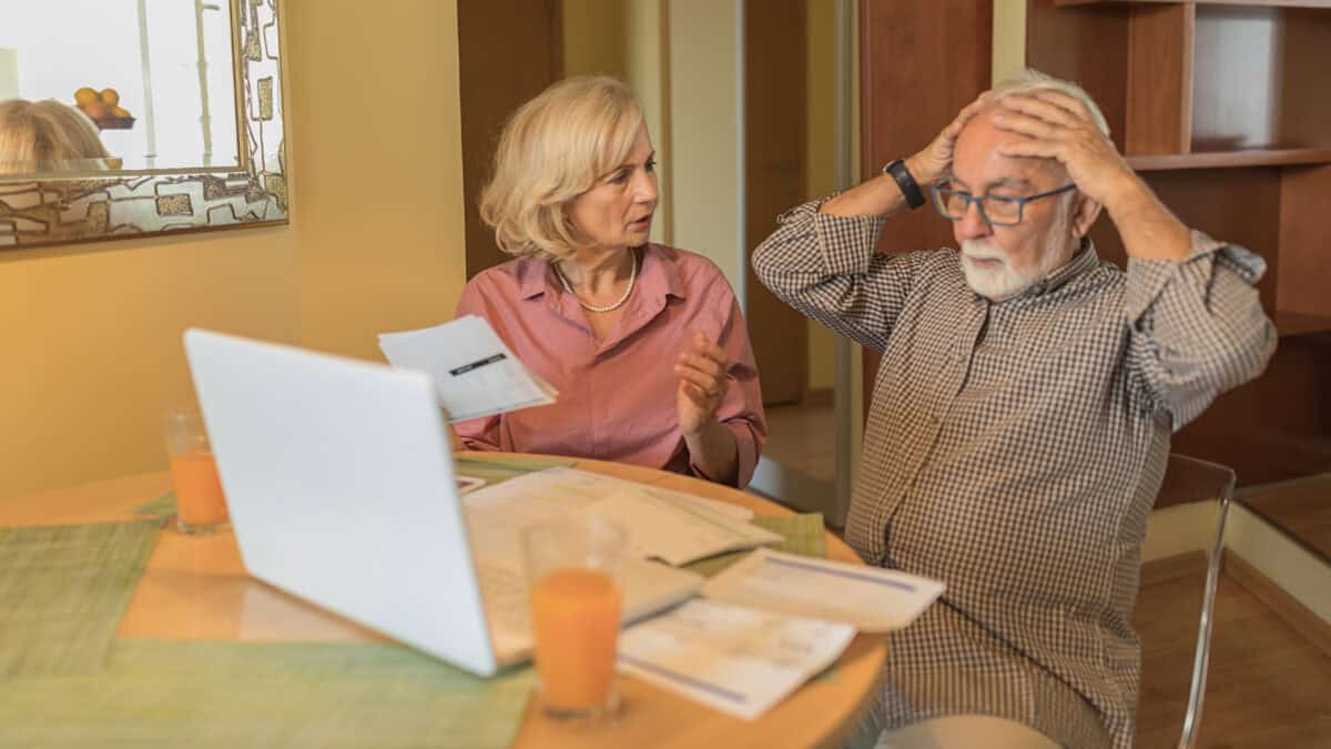 Man looking at a laptop with his hands on his head, with his partner trying to talk to him.