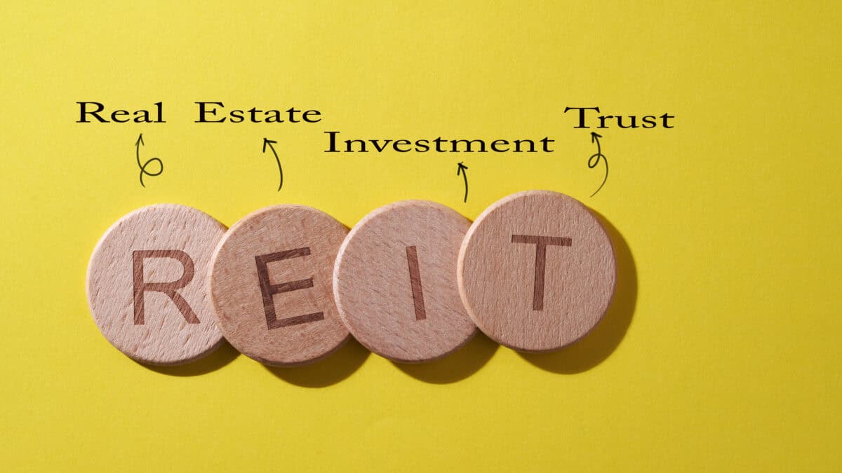 REIT on wooden circles with real estate investment trust written above on a yellow background.