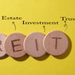 REIT on wooden circles with real estate investment trust written above on a yellow background.