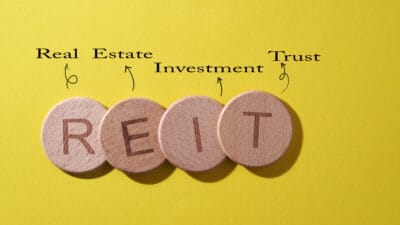 REIT on wooden circles with real estate investment trust written above on a yellow background.