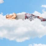 Woman dreaming and sleeping on a cloud up in the sky.