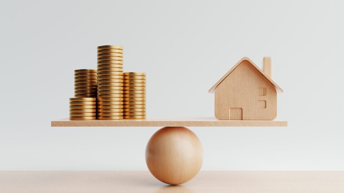 Wooden house and golden coins on balancing scale.