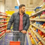 Man looking at the side of an aisle at items in a grocery store.