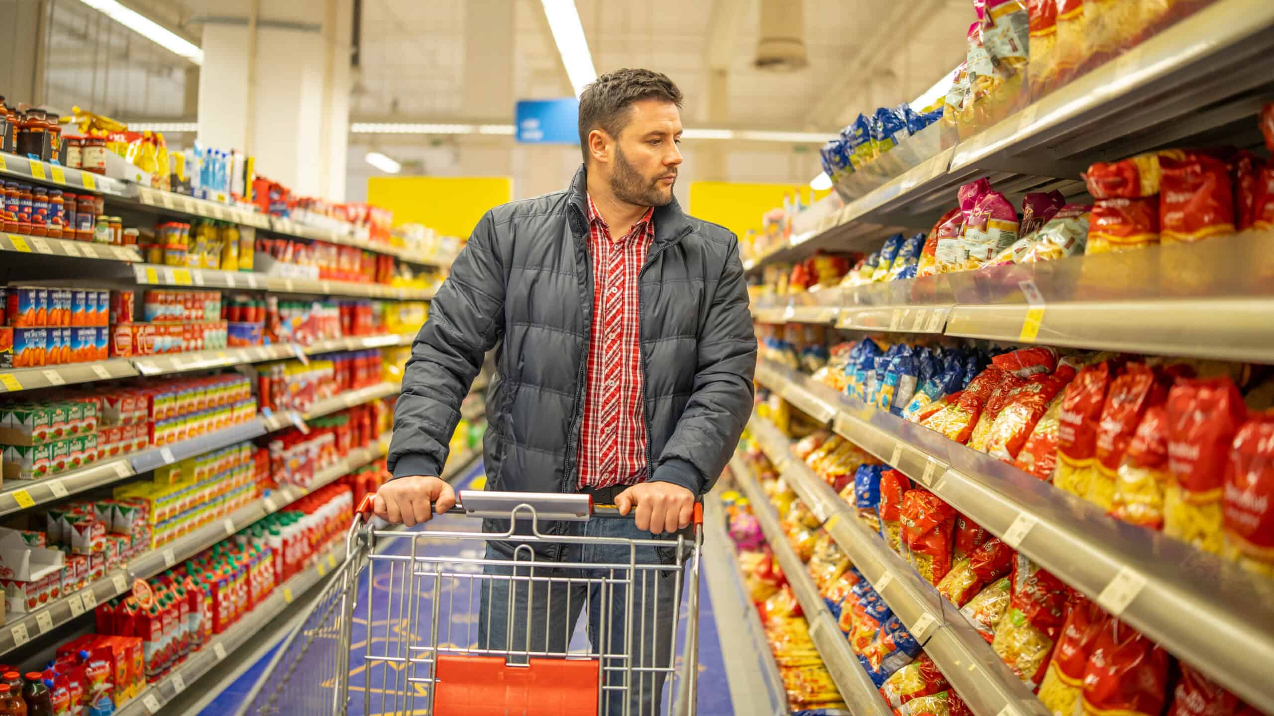 Man looking at the side of an aisle at items in a grocery store.