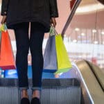 Woman's legs with colourful shopping bags on the escalator in a shopping mall.