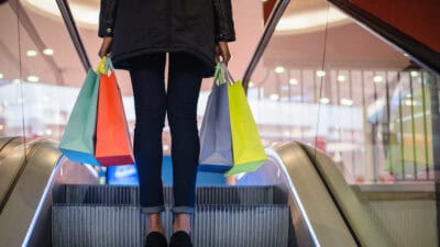 Woman's legs with colourful shopping bags on the escalator in a shopping mall.