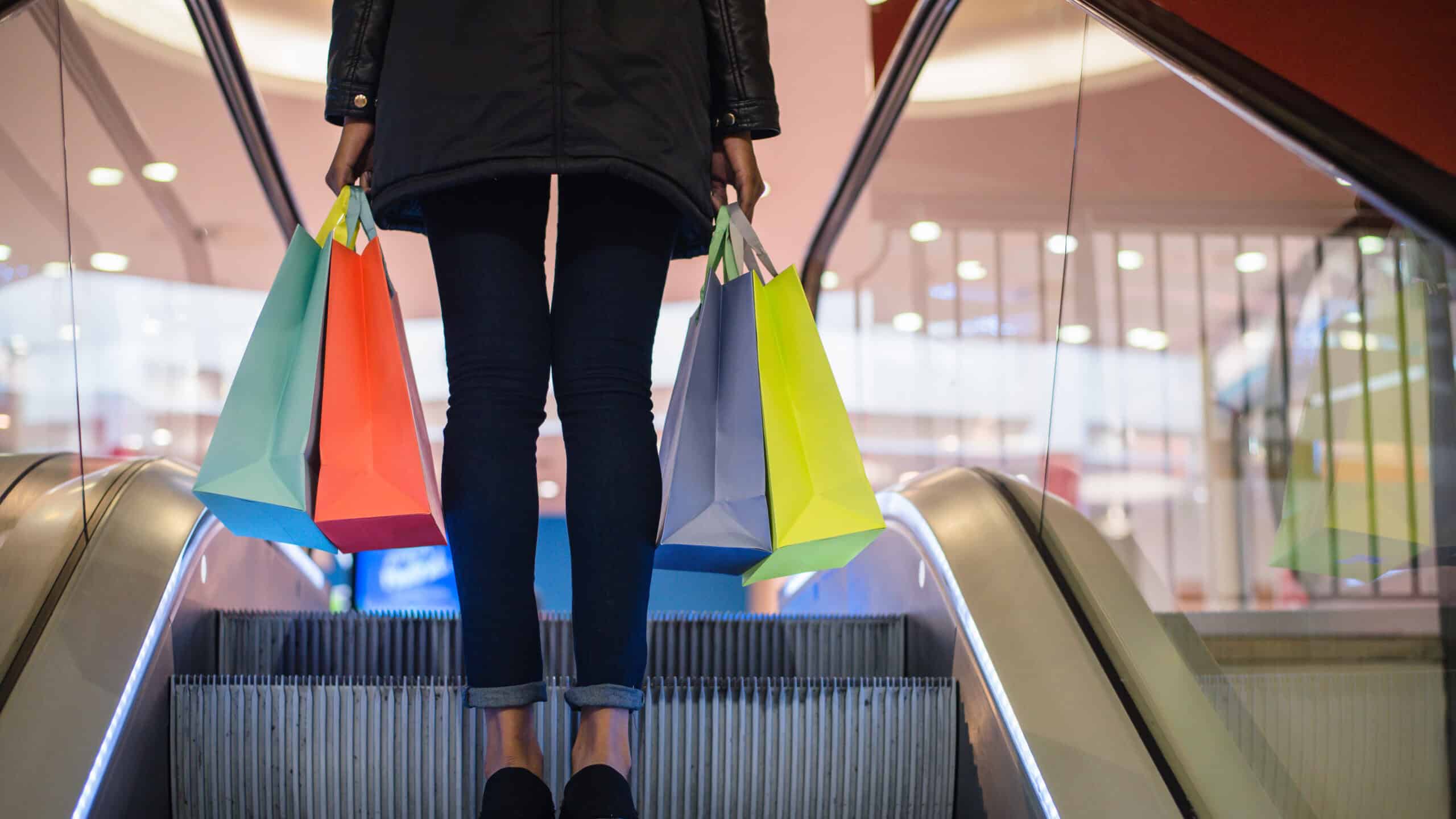 Woman's legs with colourful shopping bags on the escalator in a shopping mall.