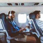 Man on a plane using a laptop with headphones on.