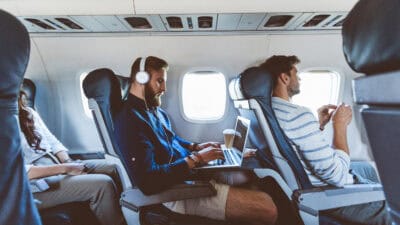 Man on a plane using a laptop with headphones on.