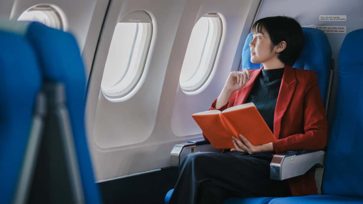 Woman looking through an airplane window while holding a book.