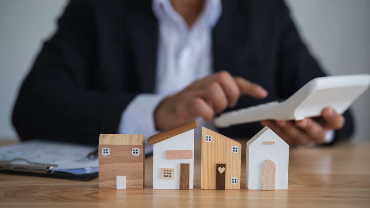 Wooden house models on a table with a man using a calculator.