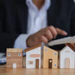 Wooden house models on a table with a man using a calculator.