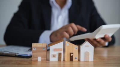 Wooden house models on a table with a man using a calculator.