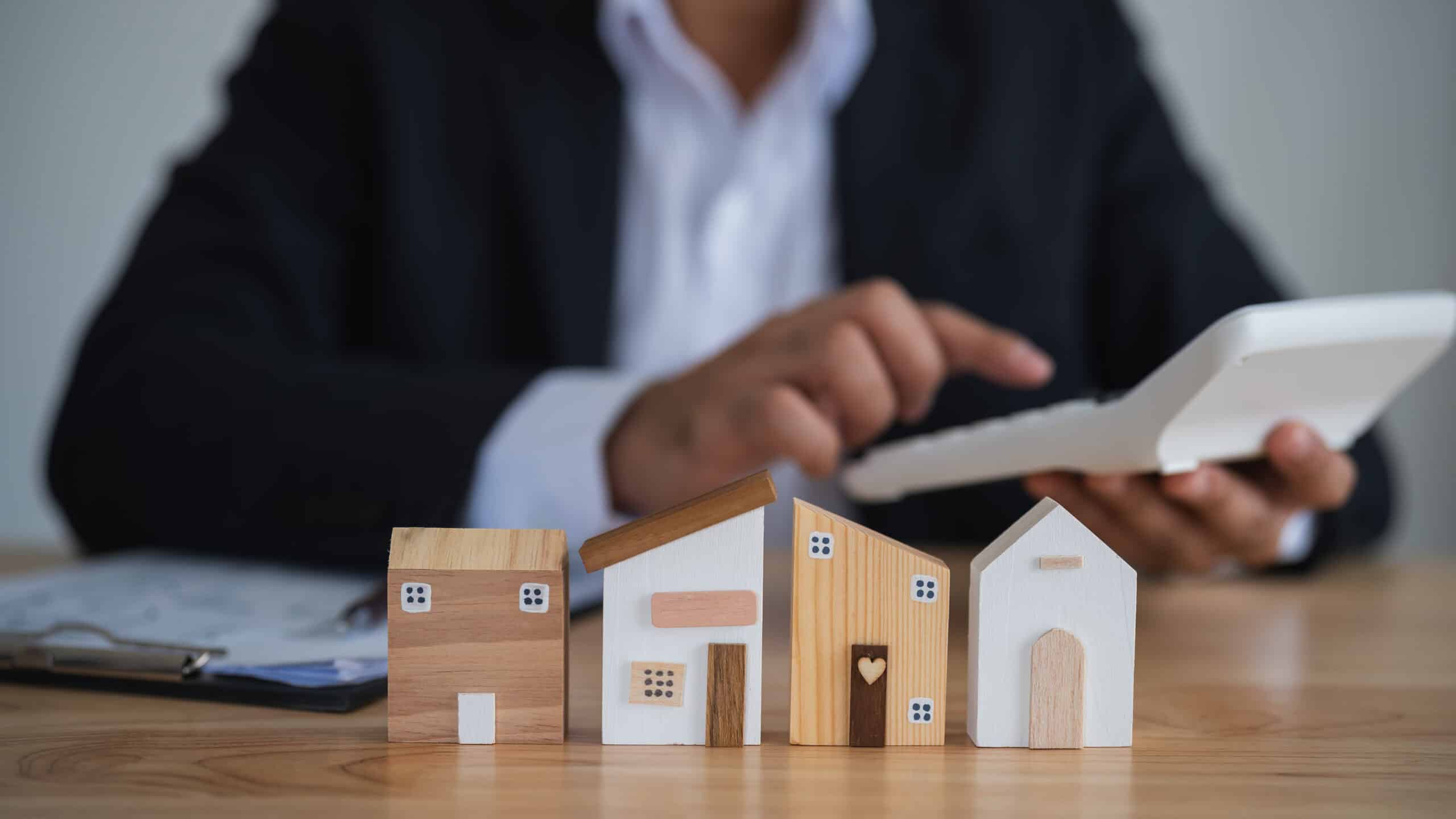 Wooden house models on a table with a man using a calculator.