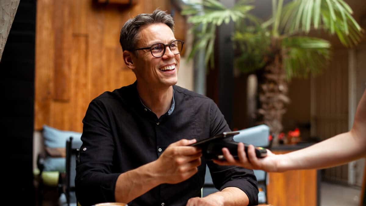 Smiling man paying for his order from his phone on an EFTPOS machine at a restaurant.