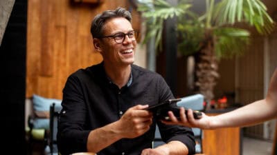 Smiling man paying for his order from his phone on an EFTPOS machine at a restaurant.