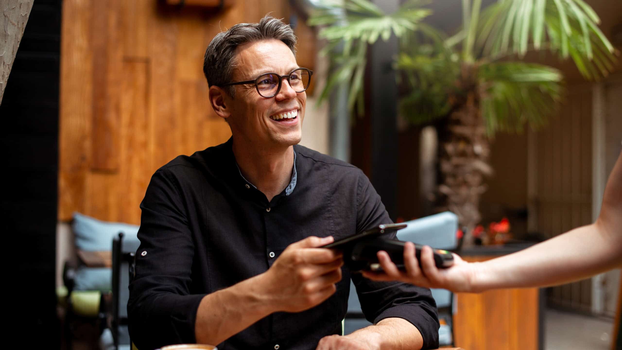 Smiling man paying for his order from his phone on an EFTPOS machine at a restaurant.