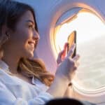 Smiling woman taking a video through a plane window with her phone.
