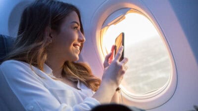 Smiling woman taking a video through a plane window with her phone.