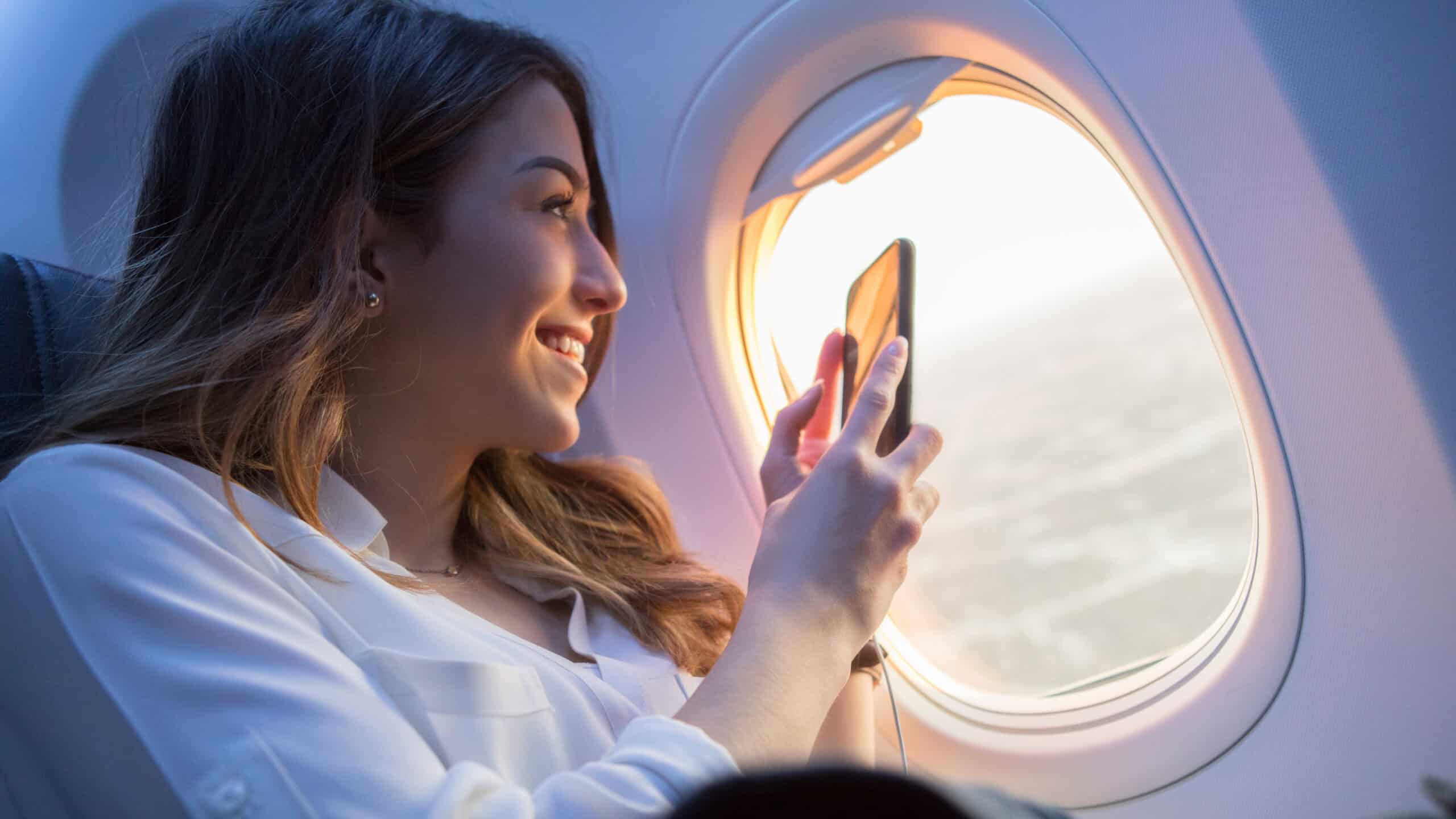 Smiling woman taking a video through a plane window with her phone.