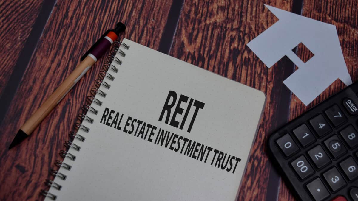 REIT and real estate investment trust written on a notebook with a pen, paper house, and calculator around it.