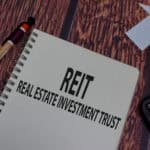 REIT and real estate investment trust written on a notebook with a pen, paper house, and calculator around it.