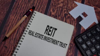 REIT and real estate investment trust written on a notebook with a pen, paper house, and calculator around it.