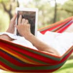 Senior woman relaxing in a hammock with an e-book on her tablet.