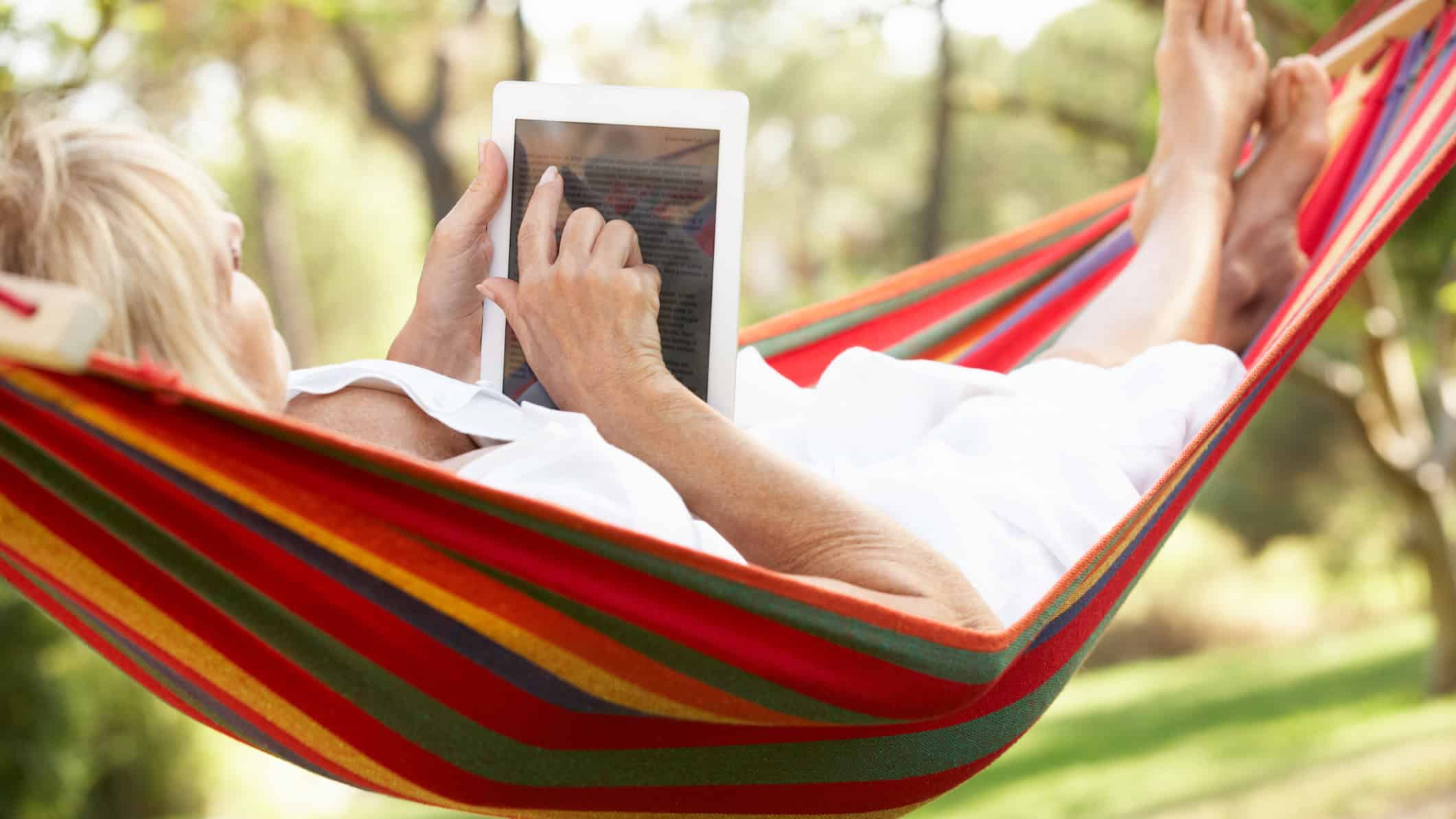 Senior woman relaxing in a hammock with an e-book on her tablet.